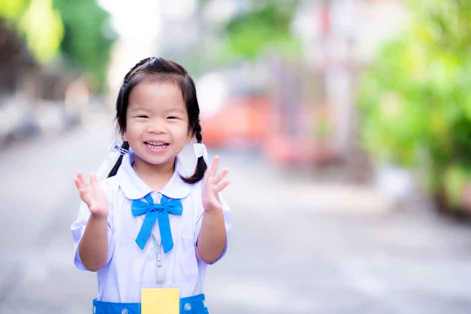 Smiling young girl in a school uniform clapping her hands—representing joyful communication and the success of speech therapy in Phnom Penh.