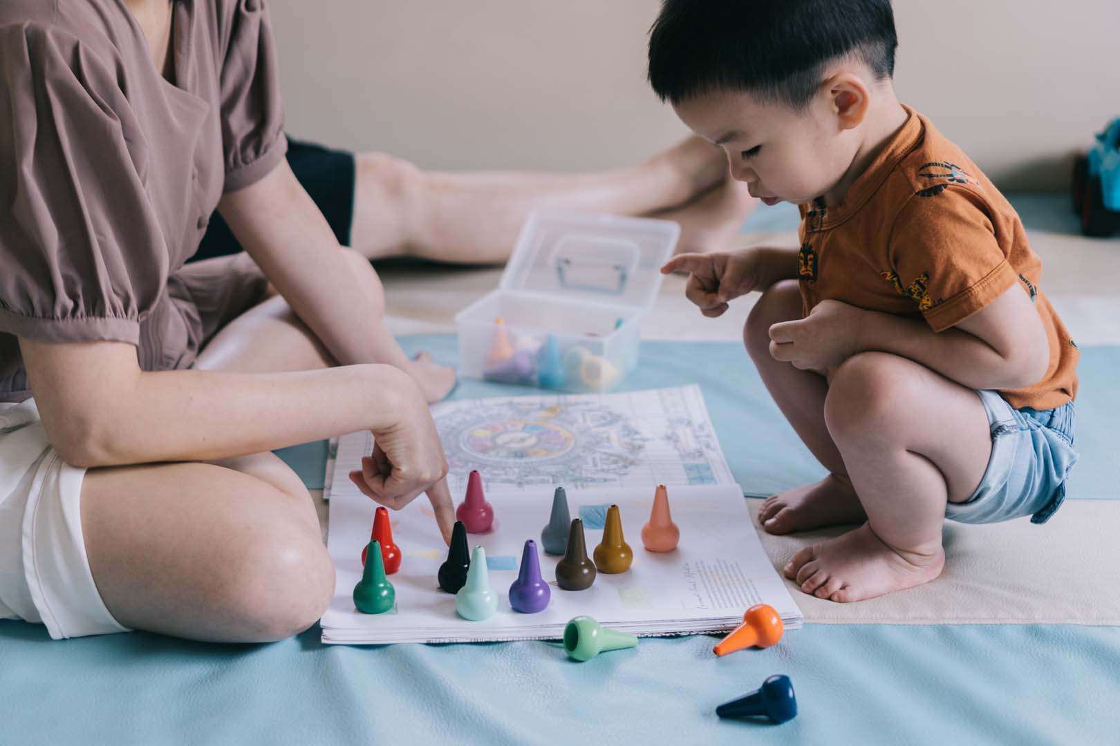 A toddler squatting while identifying and sorting colorful crayons during a guided activity, supporting speech and language development through play.