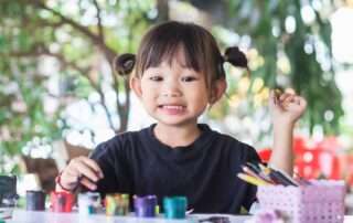 Young child smiling and painting during art-based occupational therapy session at OrbRom Center in Phnom Penh.
