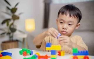 Young child developing fine motor and problem-solving skills with colorful building toys during occupational therapy at OrbRom Center in Phnom Penh.