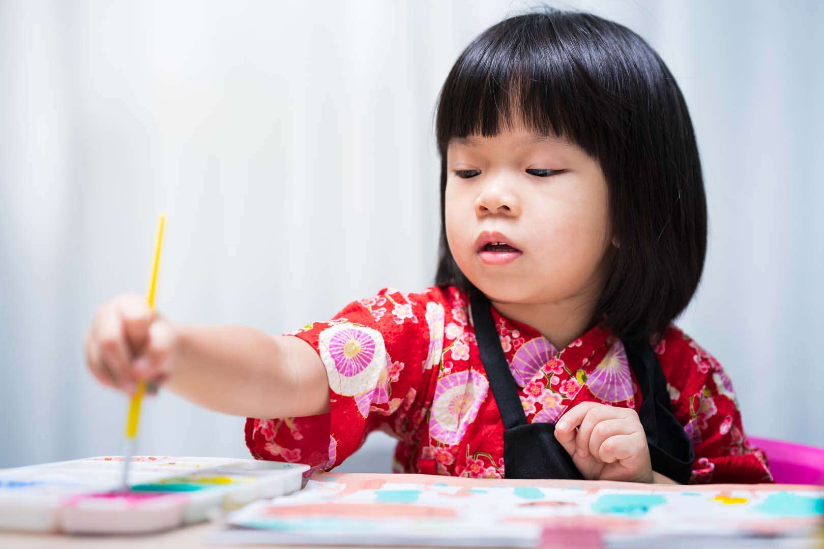 A young girl in a red outfit painting with watercolors—illustrating creative expression as a tool in speech therapy for young children.