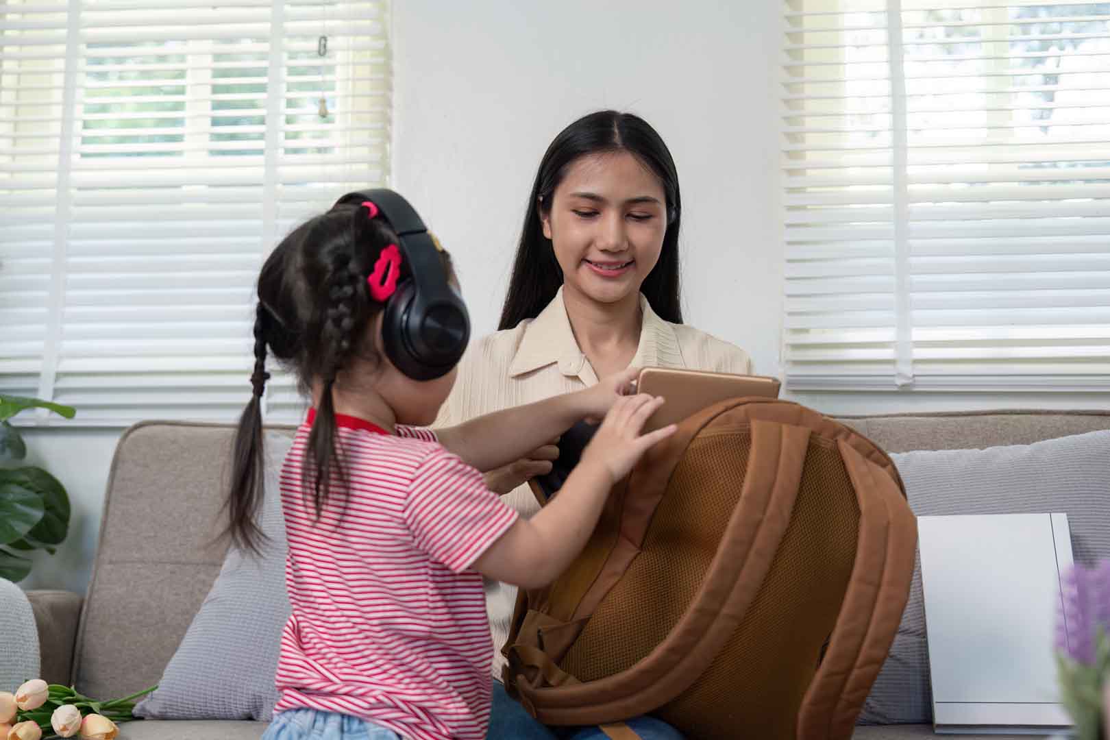 Child wearing noise-canceling headphones interacting with a caregiver during a sensory-friendly speech therapy activity in Phnom Penh