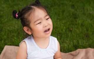 Young girl showing signs of frustration while trying to speak, sitting outdoors in Phnom Penh