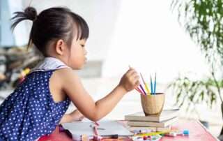 Young girl focused on choosing a paintbrush, engaged in creative drawing during an art therapy session