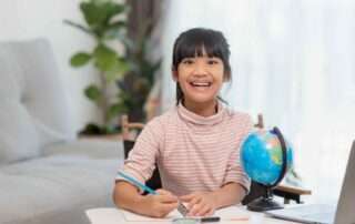 Smiling young girl learning at home with a globe and notebook, representing curiosity and global knowledge in special education.