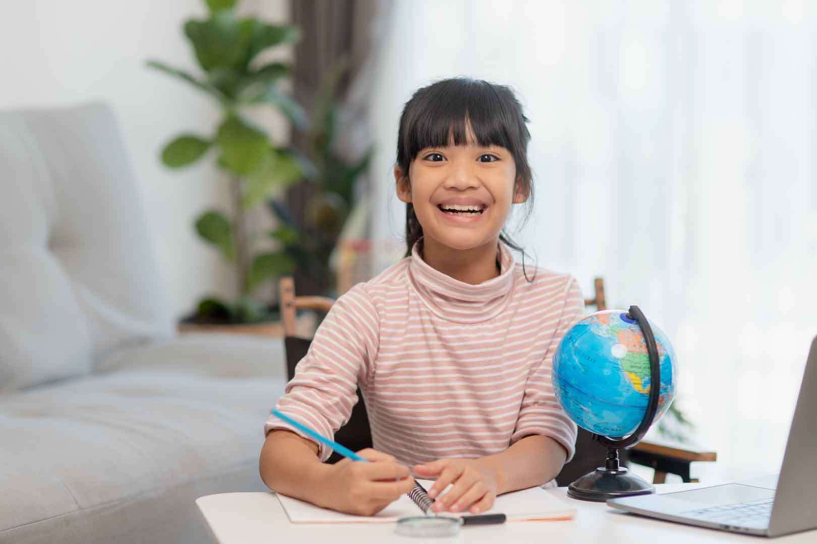 Smiling young girl learning at home with a globe and notebook, representing curiosity and global knowledge in special education.