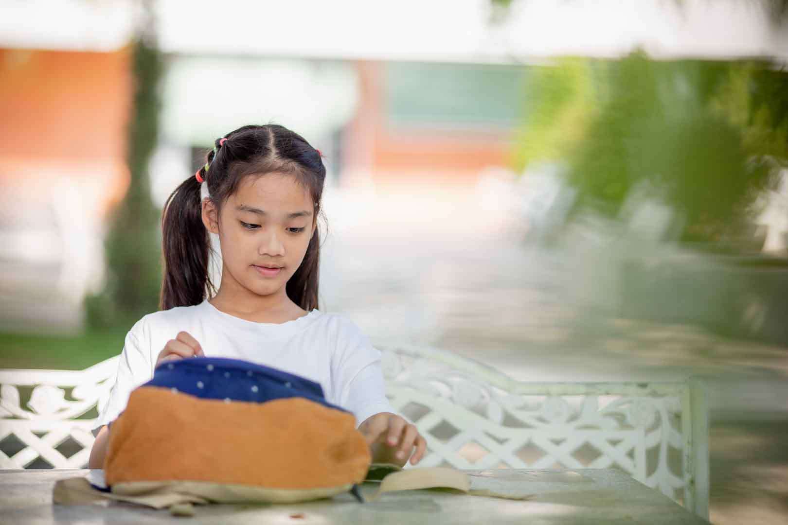Young girl organizing school materials calmly at an outdoor table, representing focus and sensory regulation.