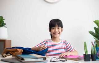 A young girl smiling at her school desk, ready for her day with organized school supplies – symbolizing independence and readiness.