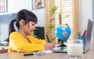 Focused young girl writing at a desk with globe and laptop, symbolizing structured learning and global curiosity.