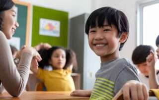Young boy smiling at his desk in a classroom, showing calm focus during a learning activity at a special needs school