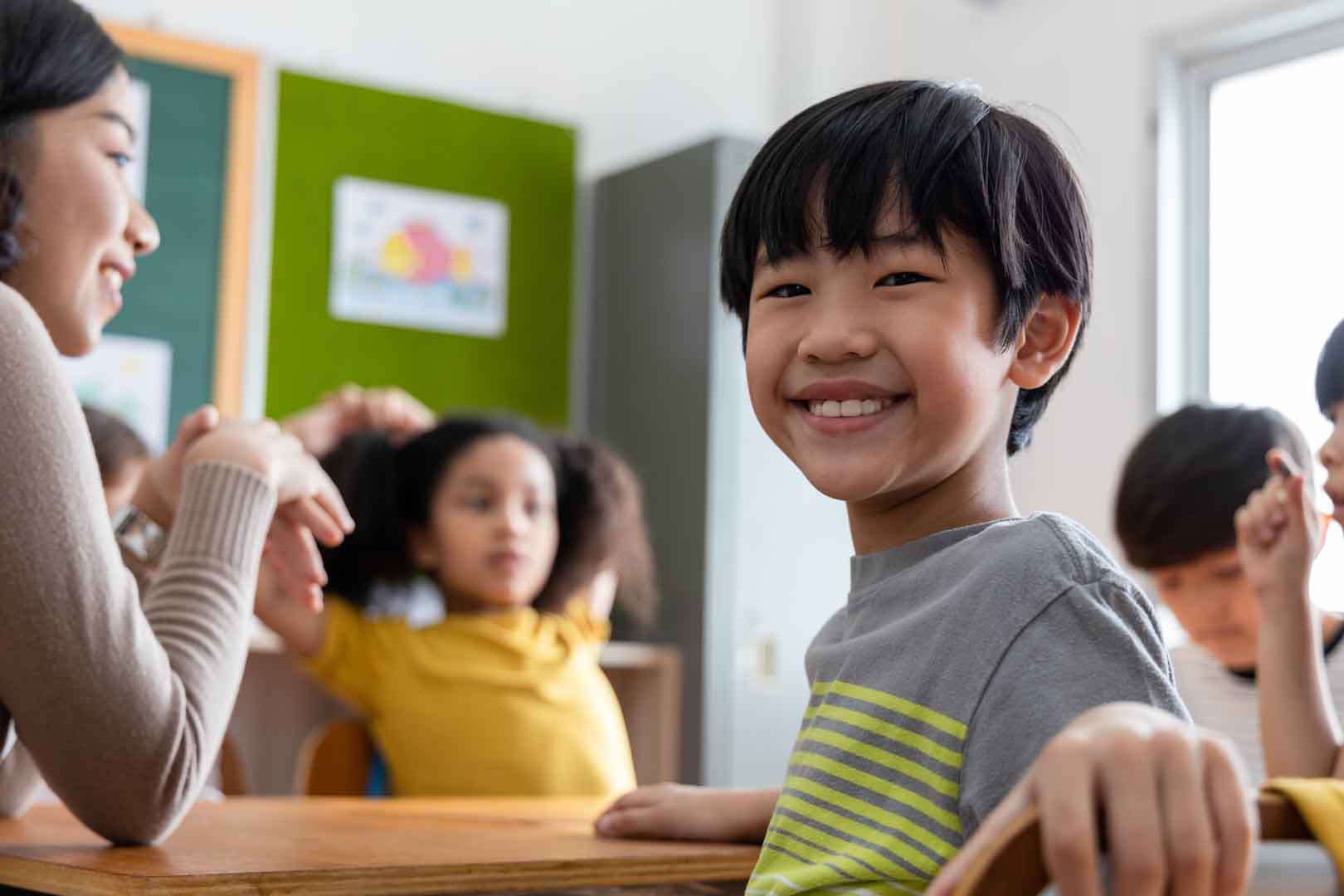 Young boy smiling at his desk in a classroom, showing calm focus during a learning activity at a special needs school
