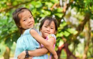 Two young girls smiling and waving during an online class, engaging in social learning and virtual interaction at home