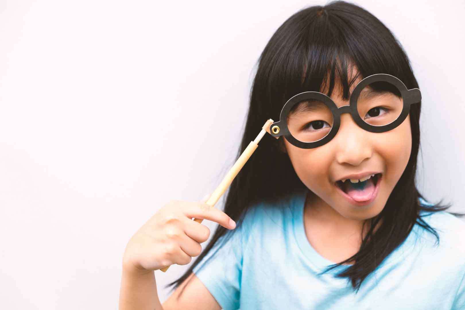Smiling young girl playfully wearing round glasses, representing joy, creativity, and social learning.